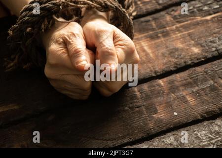 tied an old woman's hands with a rope on a wooden table, lack of will power over people, slave Stock Photo