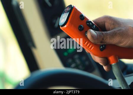 Closeup shot of red remote control with black buttons used by caucasian hand covered with dirt. Combine harvester operator. Blurred background. High quality photo Stock Photo