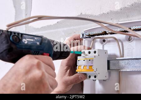 Mounting fuse box for distribution board. Fastening circuit breakers to DIN rail of consumer unit of electrical panel. Stock Photo