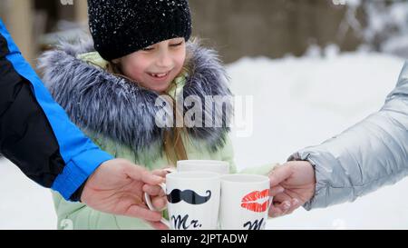 against the background of winter forest, a girl of seven years drinks tea from a cup, on the cups, sponges are drawn. Family tea in the winter forest, winter picnic. High quality photo Stock Photo