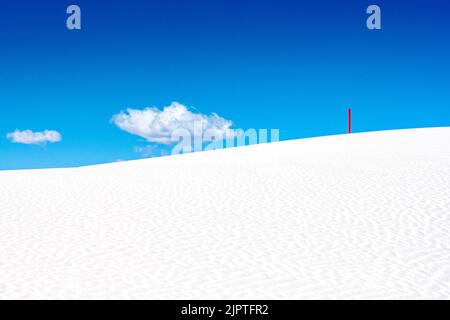 Single Red Marker Standing On White Dune With Puffy Cloud In The Sky in White Sand Dunes National Park Stock Photo