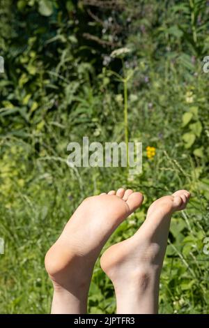 Barefoot female feet bask in the sun on a hot summer day, against the backdrop of greenery. Vacation concept.  Stock Photo
