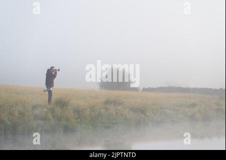 Kilmacolm, Scotland, UK, August 12th 2022, Photographer at sunrise looking for rare wildfowl on loch Stock Photo