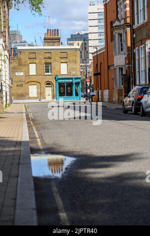 LONDON - May 20, 2022: Old chimneys on brick building and reflected in puddle on the road Stock Photo