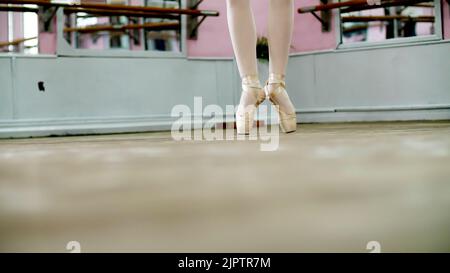 close up, in dancing hall, ballerina perform ssissonne simples , She is standing on toes in pointe shoes elegantly , on an old wooden floor, in ballet class. High quality photo