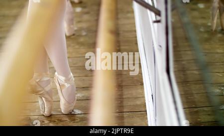 close up, in dancing hall, Young ballerinas in purple leotards perform pas de bourre suivi in the fifth position, standing on toes in pointe shoes near barre at mirror in ballet class... High quality photo Stock Photo