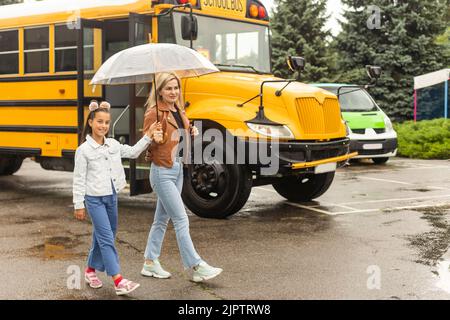 Back to school. Pupils of primary school near school bus. Happy children ready to study. little girl with mom going to bus Stock Photo