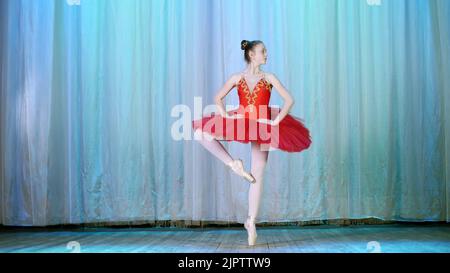 ballet rehearsal, on the stage of the old theater hall. Young ballerina in red ballet tutu and pointe shoes, dances elegantly certain ballet motion, pas courru , tour fouette. High quality photo Stock Photo