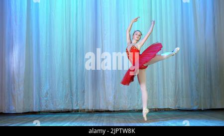 ballet rehearsal, on the stage of the old theater hall. Young ballerina in red ballet tutu and pointe shoes, dances elegantly certain ballet motion, tour fouitte. High quality photo Stock Photo