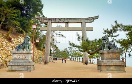 Komainu lion-dog statue in front of the stone Torii gate entrance of Itsukushima Shrine. Miyajima Island, Hiroshima Prefecture, Japan. Stock Photo