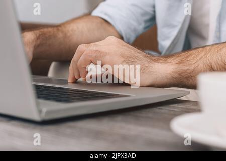 Close-up Hands of modern programmer or office manager over laptop keyboard while programming. Guy in blue shirt and white T-shirt. Cup of coffee on table. freelance Stock Photo