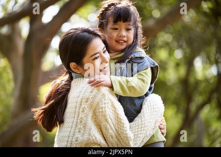loving asian mother hugging cute daughter outdoors in park happy and smiling Stock Photo