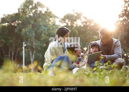 asian family with two children relaxing outdoors in city park Stock Photo