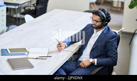 Young indian business man wearing headphones using phone at work. Stock Photo