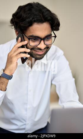 Smiling indian bank manager talking on phone consulting client using pc. Stock Photo