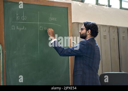 Busy indian business man working in office writing project plan on blackboard. Stock Photo