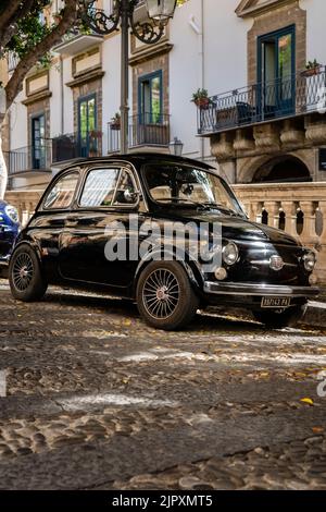 A vertical shot of an old retro black shiny FIAT parked in front of a residential building Stock Photo