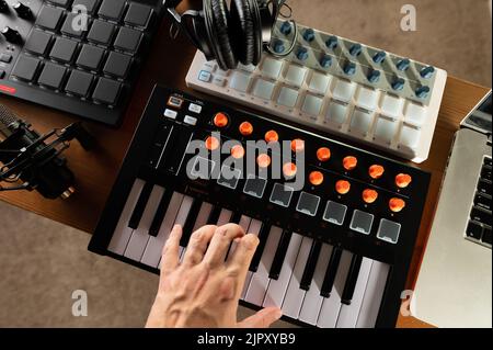Man's hand on midi keyboard. Studio headphones. Low angle view. Modern equipment for recording studio, music studio. Workplace of a musician, composer Stock Photo