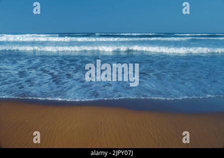 Incoming whitewater waves lapping onto sandy shore Stock Photo