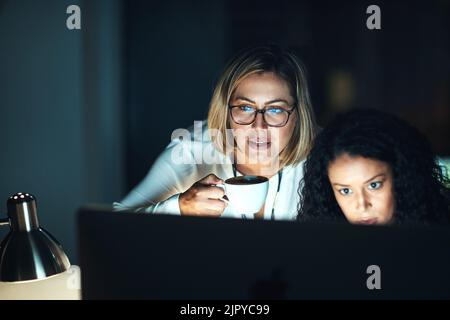 Teamwork will take them through the night. two colleagues using a computer together during a late night at work. Stock Photo