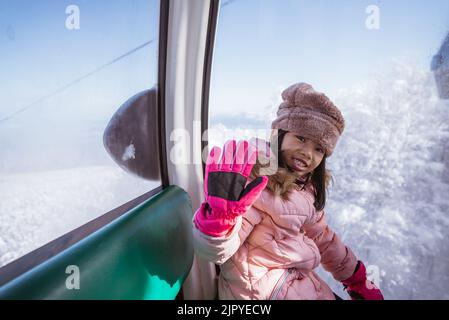 excited young girl riding a cable car going up Stock Photo