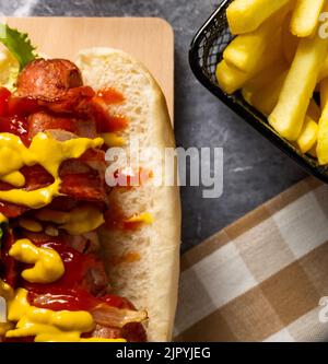 A hotdog sandwich with mustard, catsup, and fresh vegetables alongside a basket of french fries Stock Photo