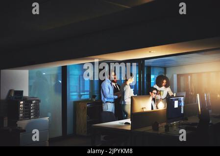 Getting efficient answers due to less time and more pressure. colleagues standing together as they work on something on a computer at night. Stock Photo