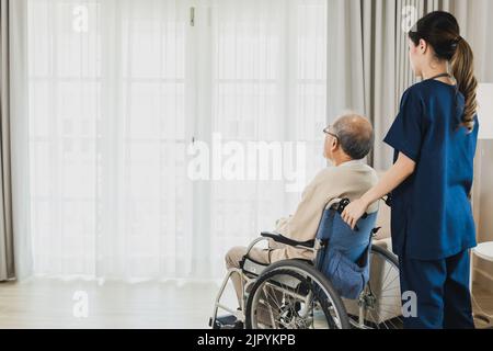 Senior Asian man in wheelchair receives medical help for injury, take care and take to looking looking out of window Stock Photo