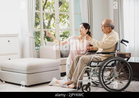 senior with beautiful daughter, old man sitting on wheelchair in house, take care elderly patient and be friends at home Stock Photo