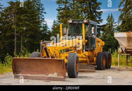 Motor Grader on road construction in forest area. Greyder leveling the sand, ground and gravel. Heavy machinery and construction equipment for grading Stock Photo