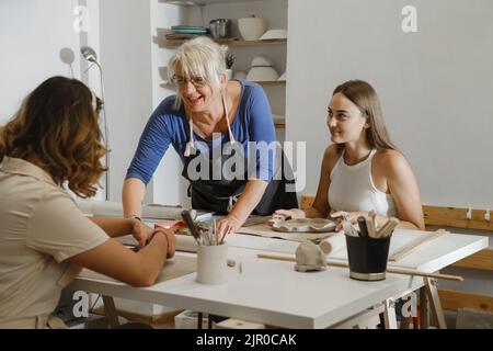 Pottery workshop in studio. People working with clay on the table. Adults learning to do ceramic plates. Pottery as hobby and leisure activity Stock Photo