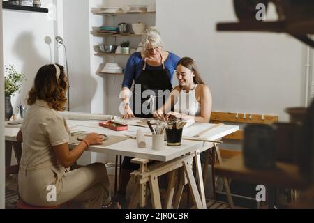 Pottery workshop in studio. People working with clay on the table. Adults learning to do ceramic plates. Pottery as hobby and leisure activity Stock Photo