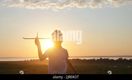 Happy boy runs on meadow playing with toy airplane at sunset Stock Photo