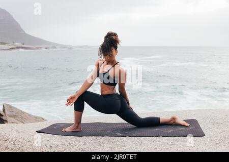 Fit woman practicing yoga by ocean. Female in yoga pose outdoors. Stock Photo