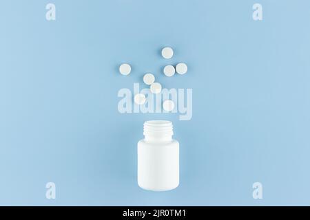 white round pills scattered from a white plastic jar on a blue background Stock Photo