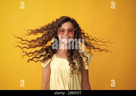 Teenager portrait with crazy movement hair. Young teen child with flowing hair. Brunette teen girl fluttering hair in motion, isolated on yellow Stock Photo