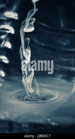 A vertical closeup shot of a transparent grey smoke on a black background Stock Photo