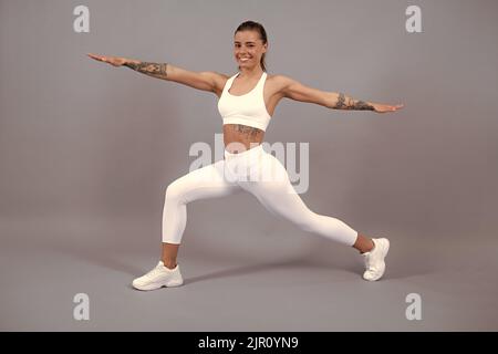 Full body of young cheerful smiling woman in sports wear, isolated over gray background. Healthy beautiful sportswoman. Stock Photo