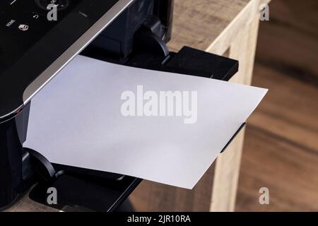 A close up portrait of a printer with an empty white piece of paper in its printed output tray. The blank page can be used to display some print out. Stock Photo