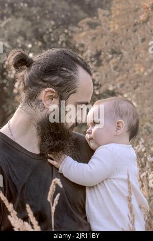 Young father holding baby in the nature. Cute imagery of baby and father together. Dad and baby looking to each other. Bearded man holding small baby Stock Photo