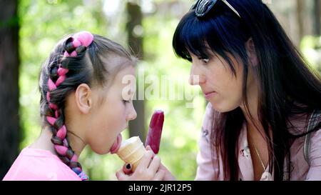 pretty girl of eight, blonde, with freckles, and her mother, a brunette woman, eating white ice cream in waffle cup , pink ice cream on stick, treat, feed each other. laugh, have fun. High quality photo Stock Photo