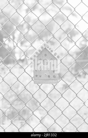 Typical common wooden birdhouse hanging on a chain link fence in the sunny summer meadow in black and white monochrome. Stock Photo