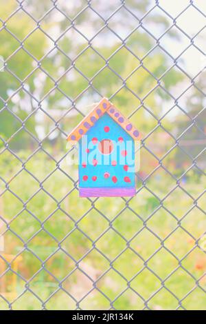 Typical common wooden birdhouse hanging on a chain link fence in the sunny summer meadow. Stock Photo