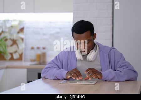 Black man using digital tablet on kitchen at home, working office work remotely typing text, African american freelancer using notepad computer Stock Photo