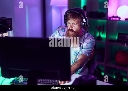 Young redhead man streamer playing video game using computer at gaming room Stock Photo