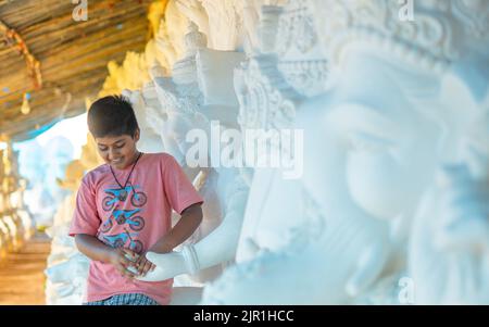 Pileru, India - July 28,2022:Kid looking down with smile holding hands of lord ganesha. Lord ganesha face next to kids face. kid holds hands with Gane Stock Photo