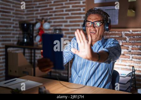 Middle age hispanic man using touchpad sitting on the table at night doing stop gesture with hands palms, angry and frustration expression Stock Photo