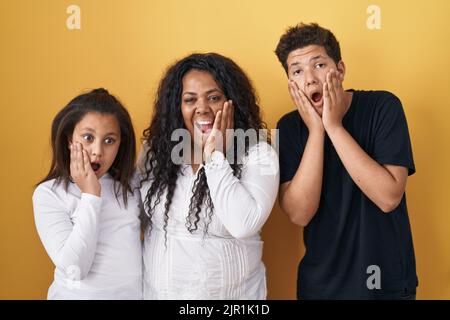 Family of mother, daughter and son standing over yellow background afraid and shocked, surprise and amazed expression with hands on face Stock Photo
