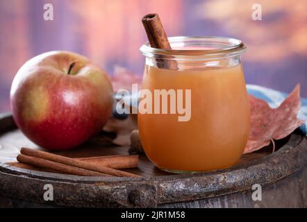 Glass of apple cider with cinnamon sticks and an apple on a wooden barrel with autumn background Stock Photo