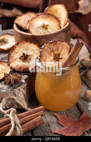 Glass of apple cider with cinnamon stick and dried apple chip on an old rustic table Stock Photo